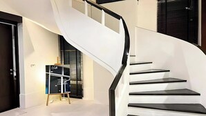 Una escalera moderna con barandilla negra y peldaños blancos, que conduce a una zona de descanso con un expositor blanco y negro.