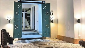 Un pasillo con una puerta verde con detalles decorativos blancos, un camino de piedra y luces en la pared.