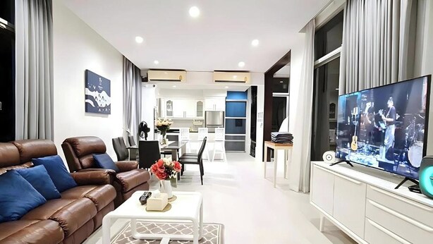 Una sala de estar moderna con un sofá de cuero marrón, una mesa de centro blanca y un televisor sobre un mueble blanco.