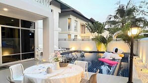 Un área de comedor al aire libre con piscina, sillas blancas y una mesa dispuesta para dos.
