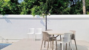 Un patio exterior con una mesa, sillas, una piscina y un farol.