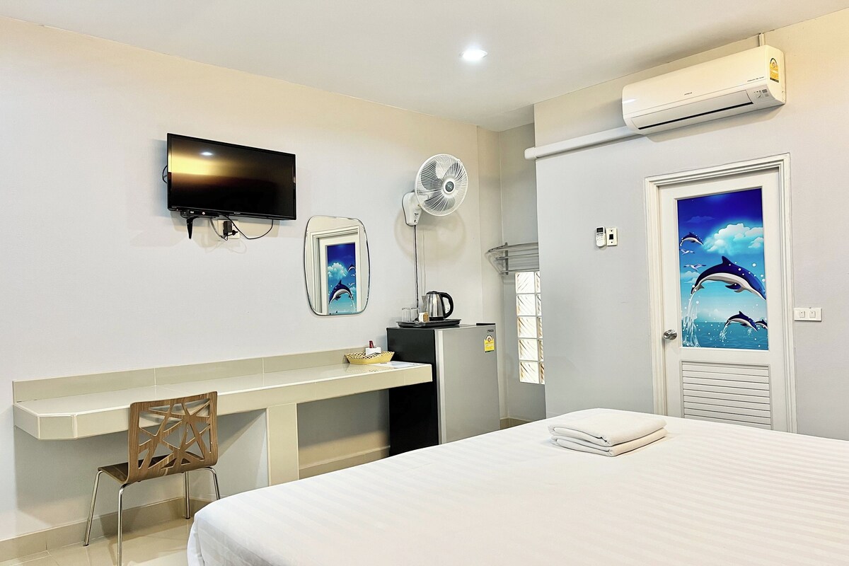 A hotel room with a bed, a desk, a chair, a TV, a fan, and a door with a dolphin mural.