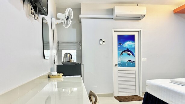 Una habitación de hotel con una cama, una mesa de comedor, un ventilador, aire acondicionado y una puerta decorada con un cuadro.