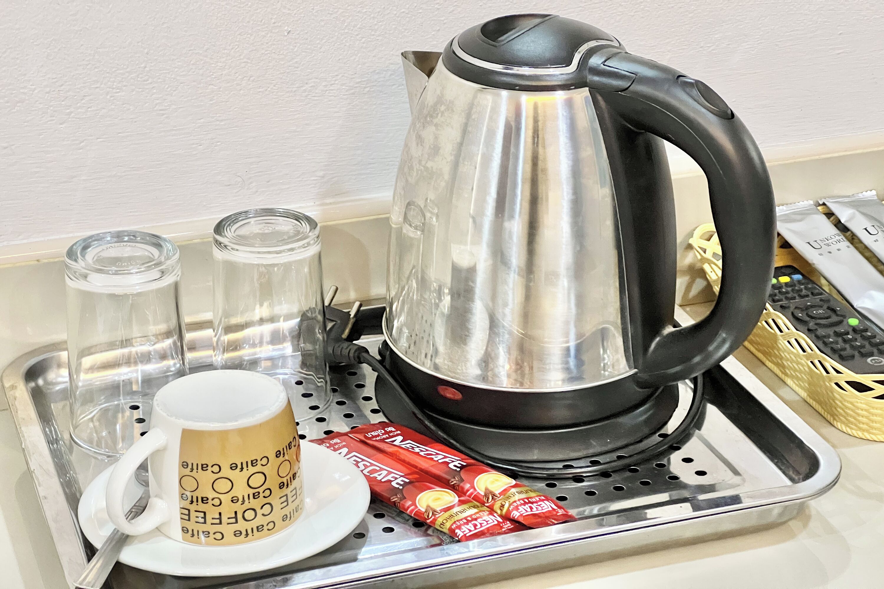 A stainless steel tray with a coffee pot, two glass cups, a coffee mug, and two packets of Nescafe instant coffee.
