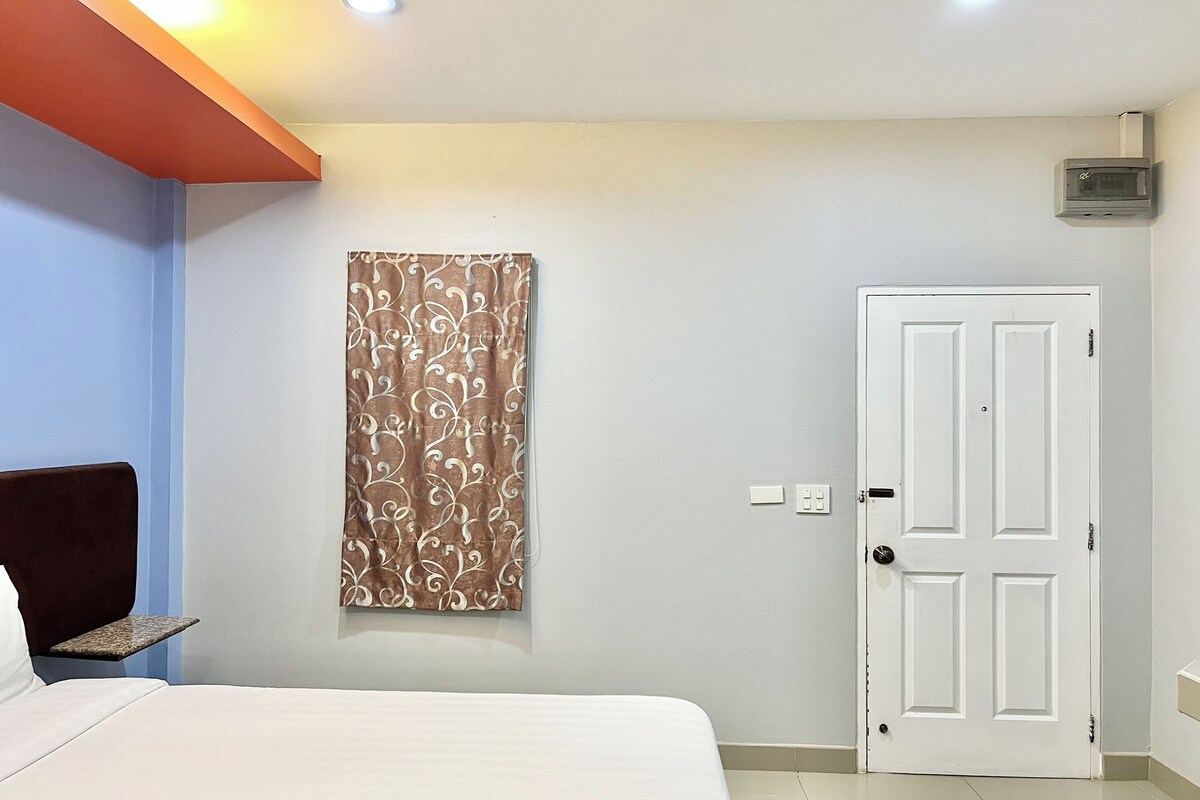 A bedroom with a bed, a headboard, a wall-mounted air conditioning unit, a door, and a light switch.