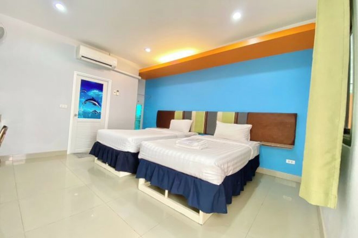 A hotel room with two beds, a blue accent wall, and an air conditioning unit.