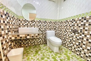 A bathroom with a checkered mosaic tile wall, a white toilet, a white sink with a marble countertop, and a green floral-patterned floor. - Full House Udon (Udon Thani)