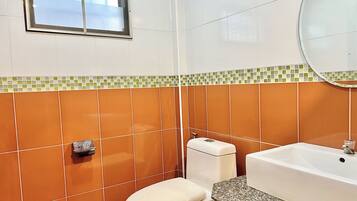 A bathroom with orange tiles, a white toilet, a sink with a mirror, and a window above the toilet.