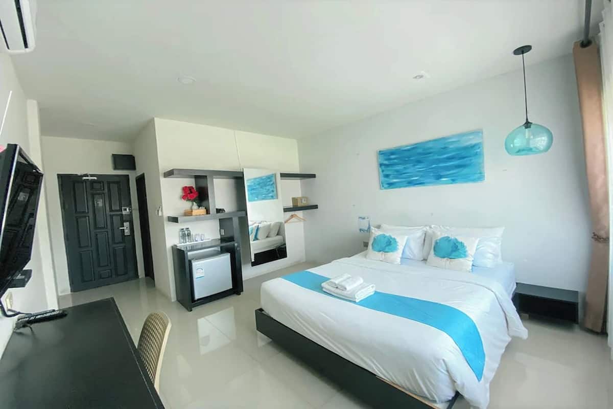 A modern hotel room with a bed, a desk, a small kitchenette, and a TV.