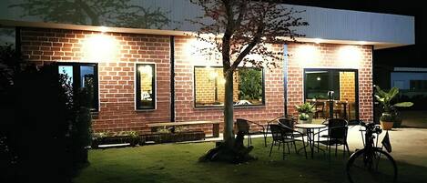 A modern building with brick walls and large windows, outdoor seating area with chairs and tables, and a bicycle parked nearby.