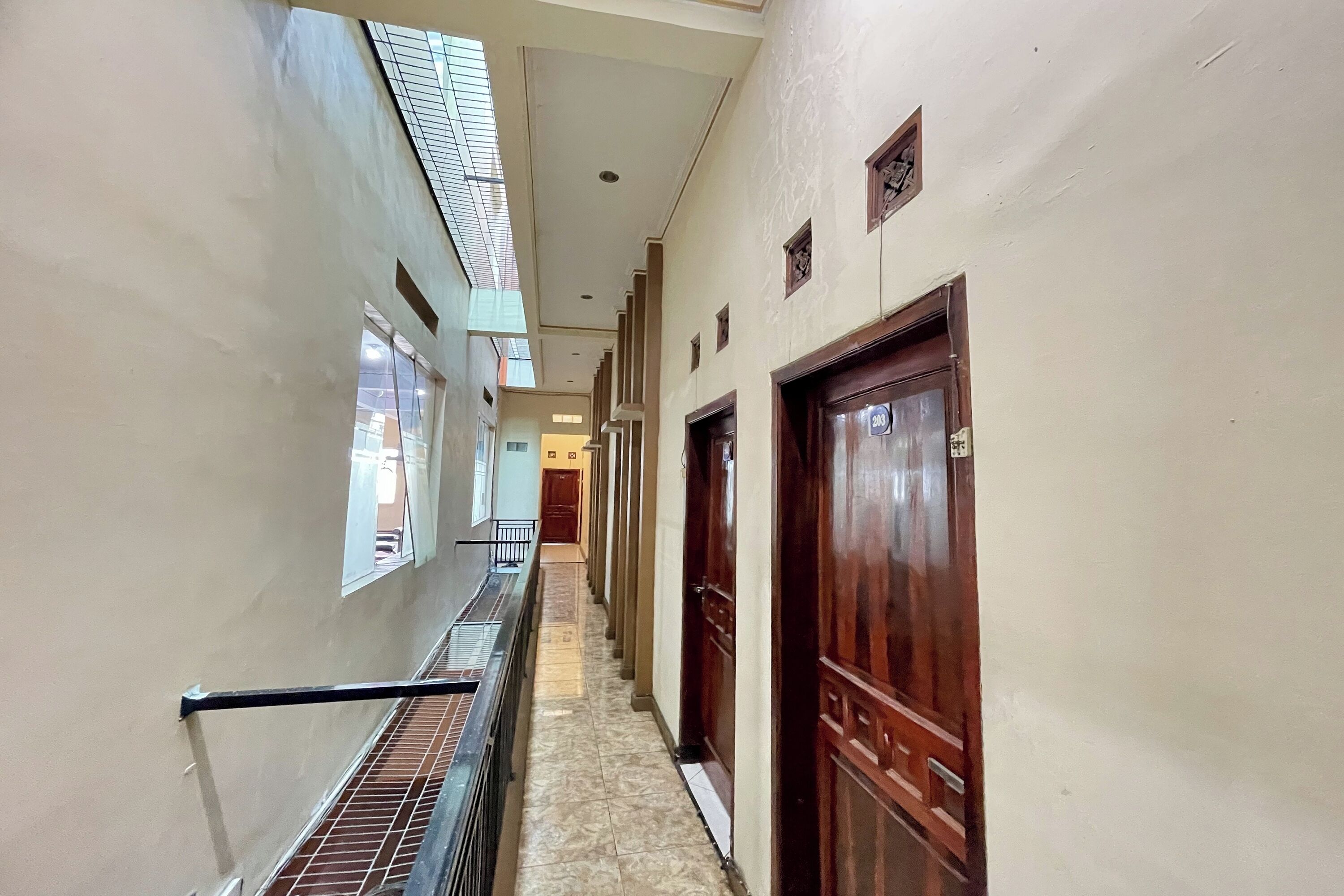 A corridor with a metal railing, wooden doors, and a tiled floor.