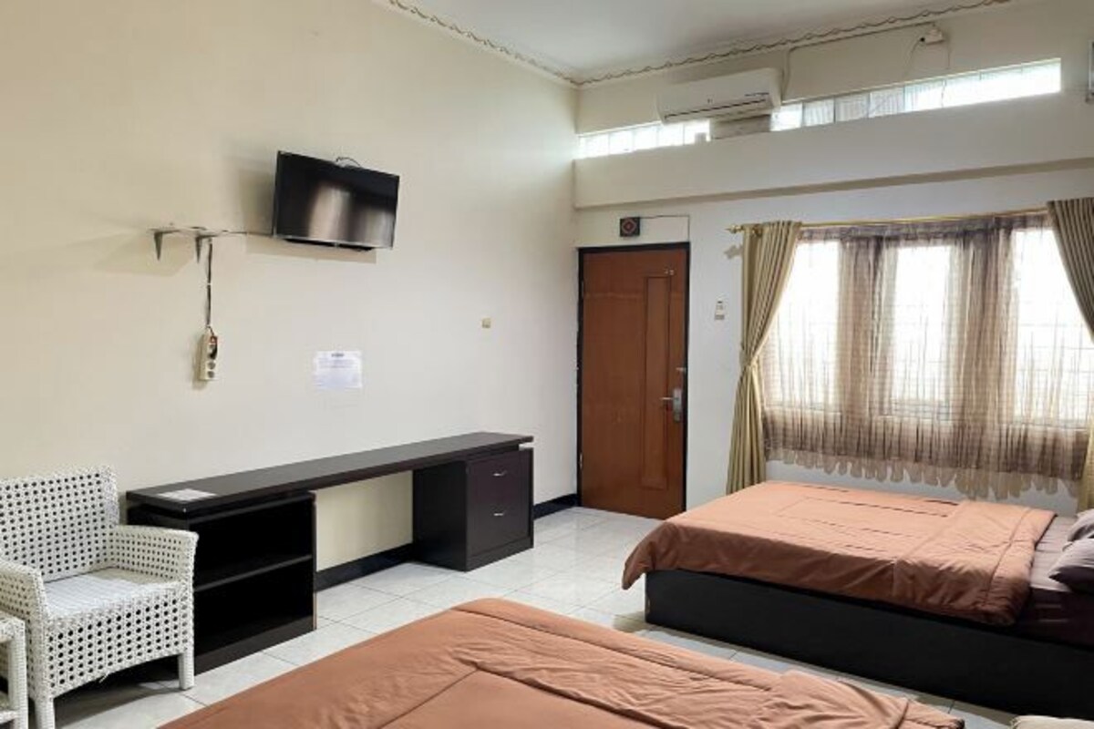 A room with a bed, a desk, a chair, a television, and a window with curtains.