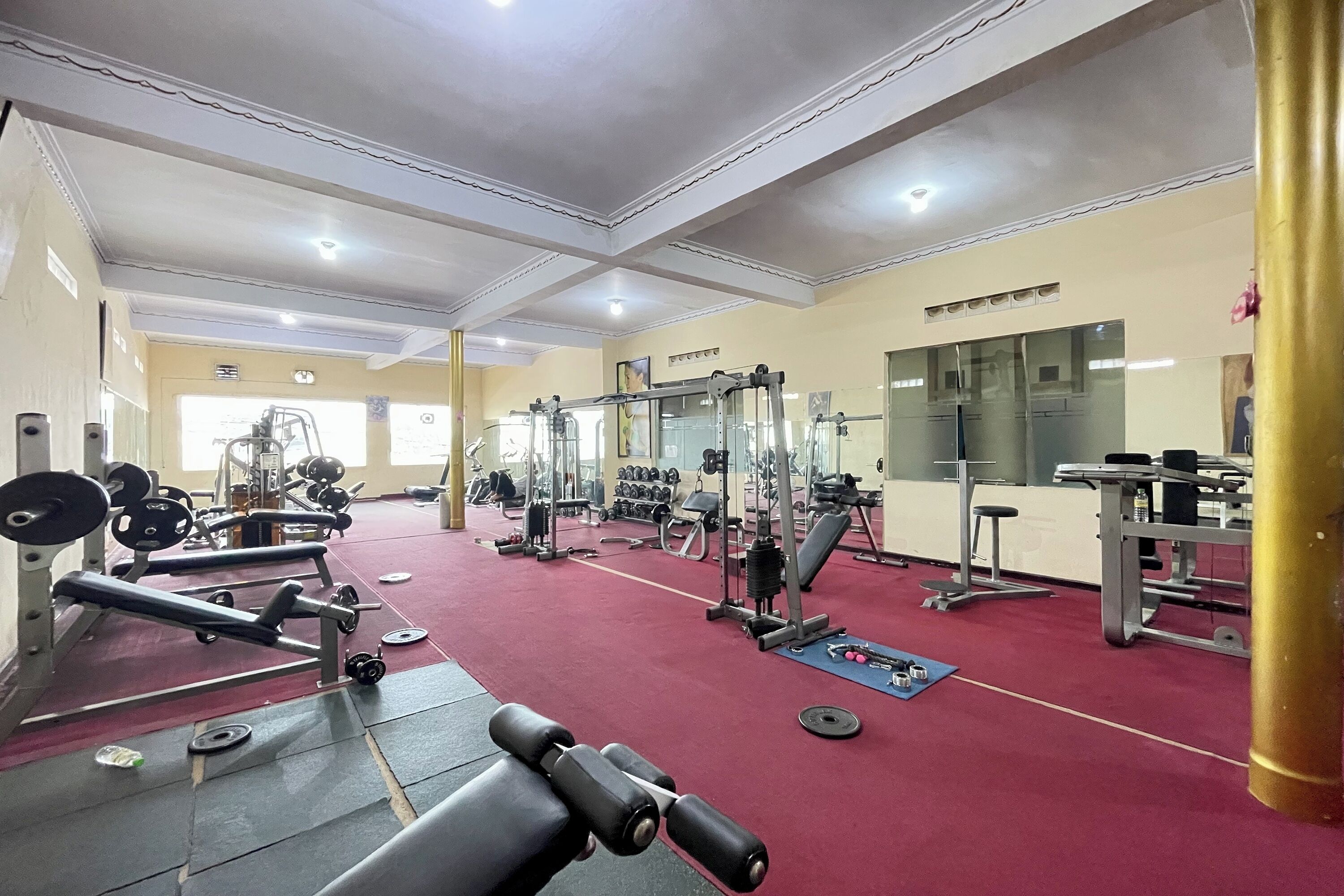 A gym with various exercise equipment, a red carpet floor, and a white ceiling with recessed lighting.