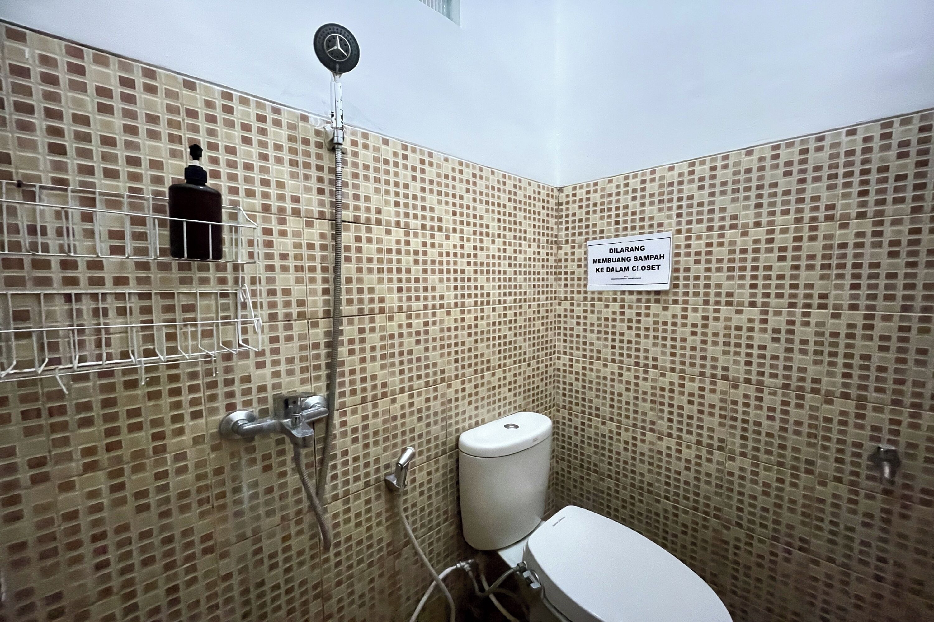 A bathroom with a tiled wall, a toilet, a shower, and a sign indicating the location.