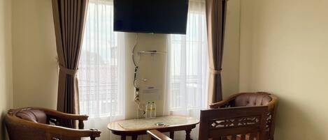 A room with a television mounted on the wall, a wooden table with two chairs, and a window with curtains.