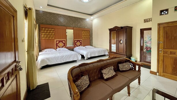 A hotel room with two beds, a sofa, a wardrobe, and a door with a decorative mirror. - Hotel Ramayana Garut (Garut)