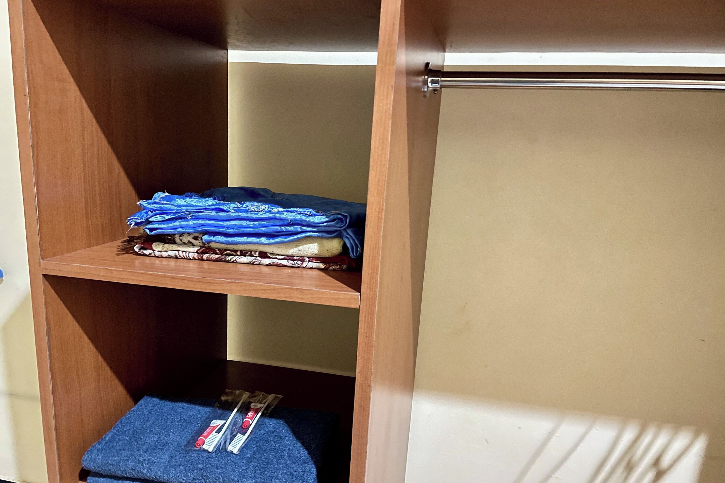 A wooden wardrobe with a shelf containing folded clothes and a blue mat with a toothbrush and toothpaste.