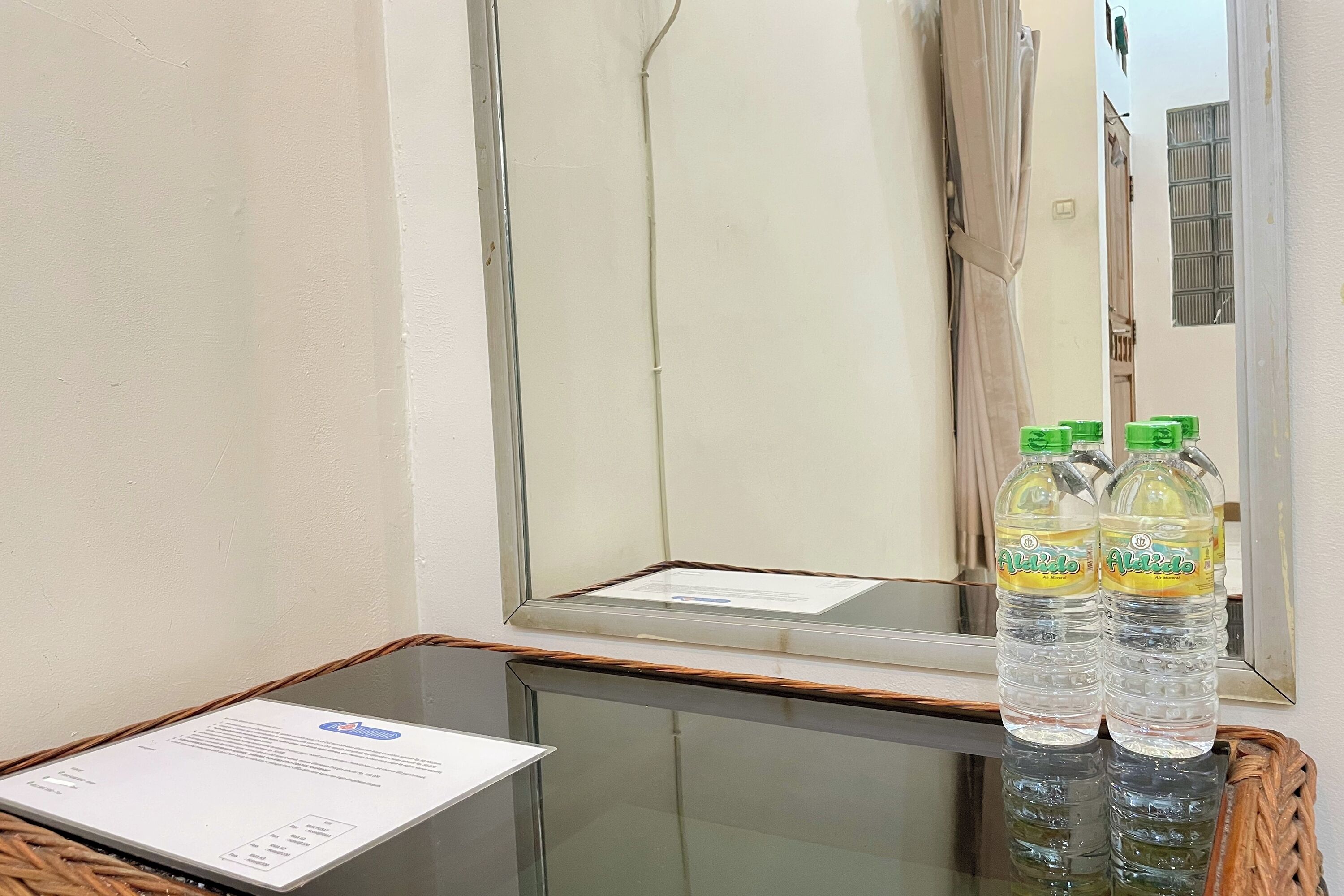 A room with a glass table, two water bottles, a framed certificate, and a mirror reflecting a door and window.