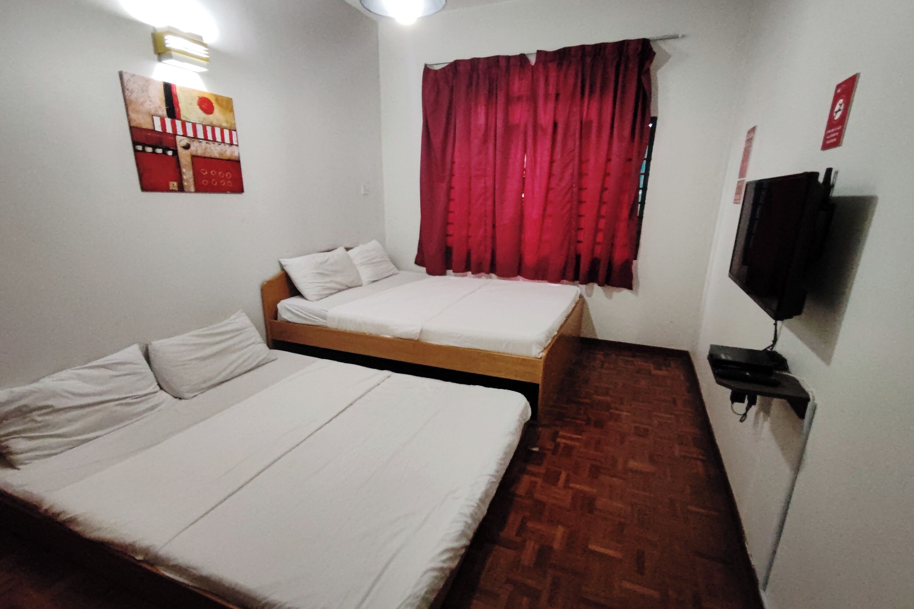 Een kamer met een bed, een klein tafeltje, een tv aan de muur en een rood gordijn.