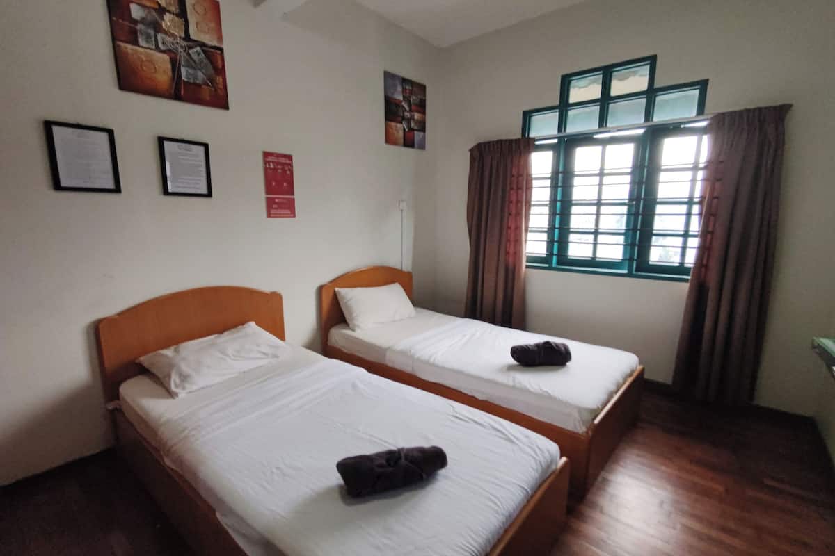 A room with two single beds, wooden headboards, white bedding, a window with curtains, and wall-mounted artwork.