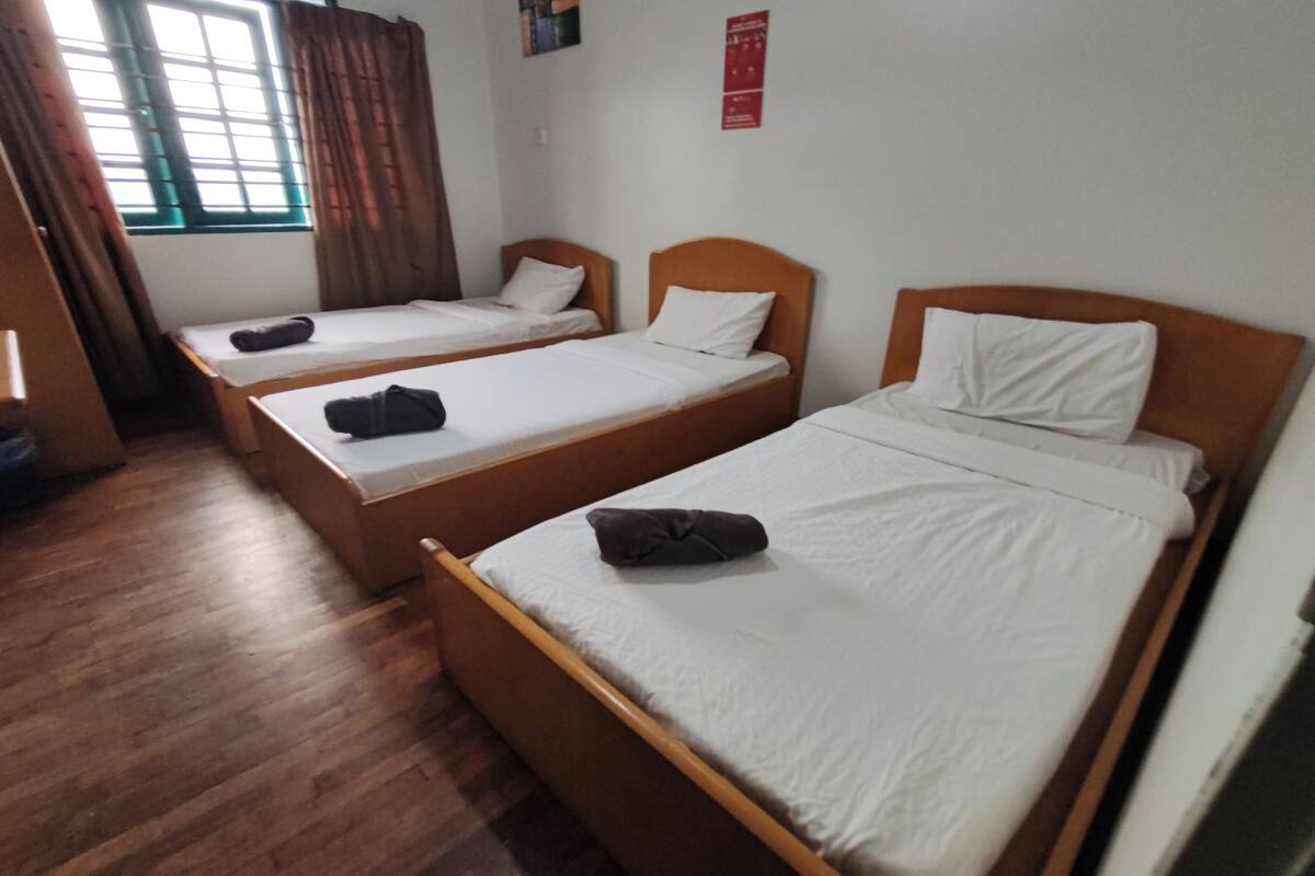 A room with three single beds, wooden headboards, and a window with curtains.