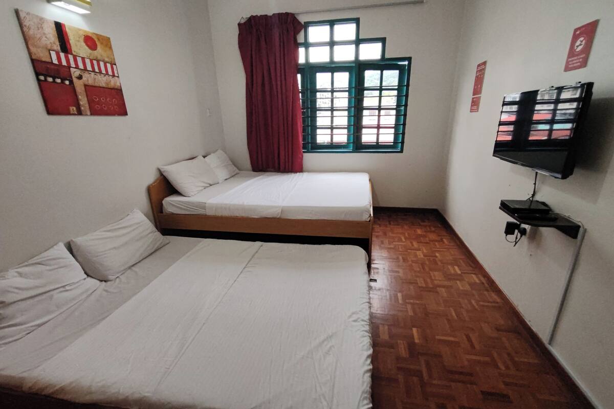 A room with two beds, a window with curtains, a wooden floor, and a mounted television.