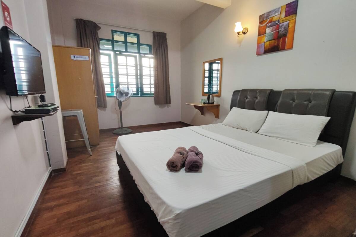 A hotel room with a large bed, a TV, a desk, and a window with curtains.