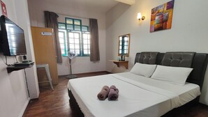 Ein Hotelzimmer mit einem großen Bett, einem Fernseher, einem Schreibtisch und einem Fenster mit Vorhängen.