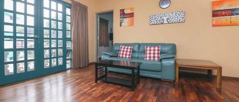 A living room with a teal sofa, a black coffee table, and a wooden bench. There are two red and white checkered pillows on the sofa. The room has a wooden floor and a large window with multiple panes.