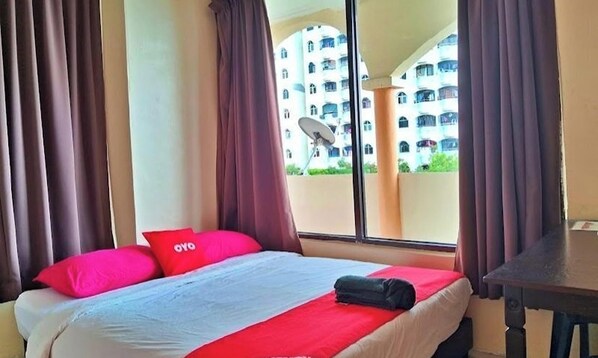 A hotel room with a bed, a window with curtains, and a view of a building with balconies. - Feringghi Stay Iinn (George Town)