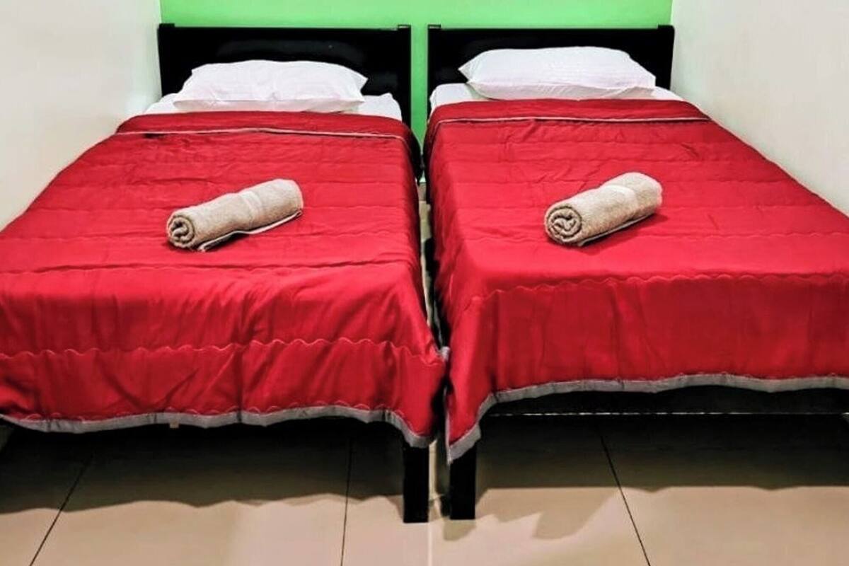 Two single beds with red bedding and white pillows, a green wall, and a tiled floor.