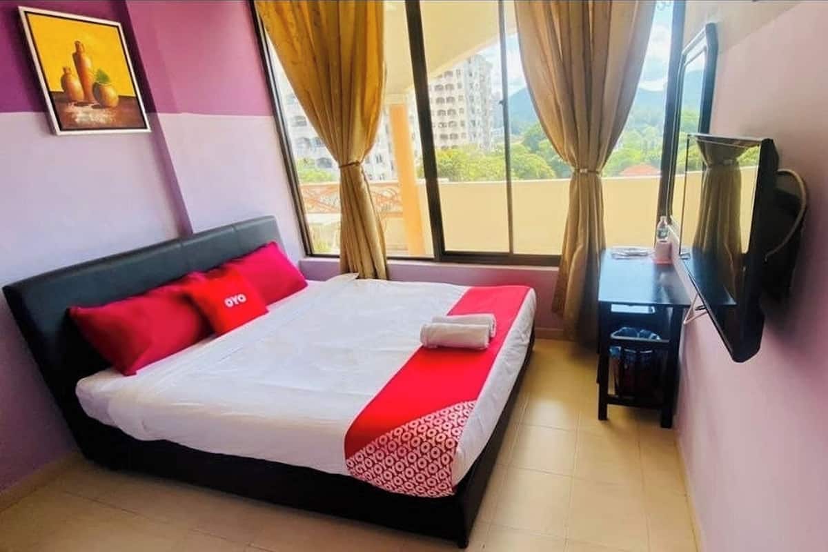 A hotel room with a bed, a desk, a TV, and a window with curtains.