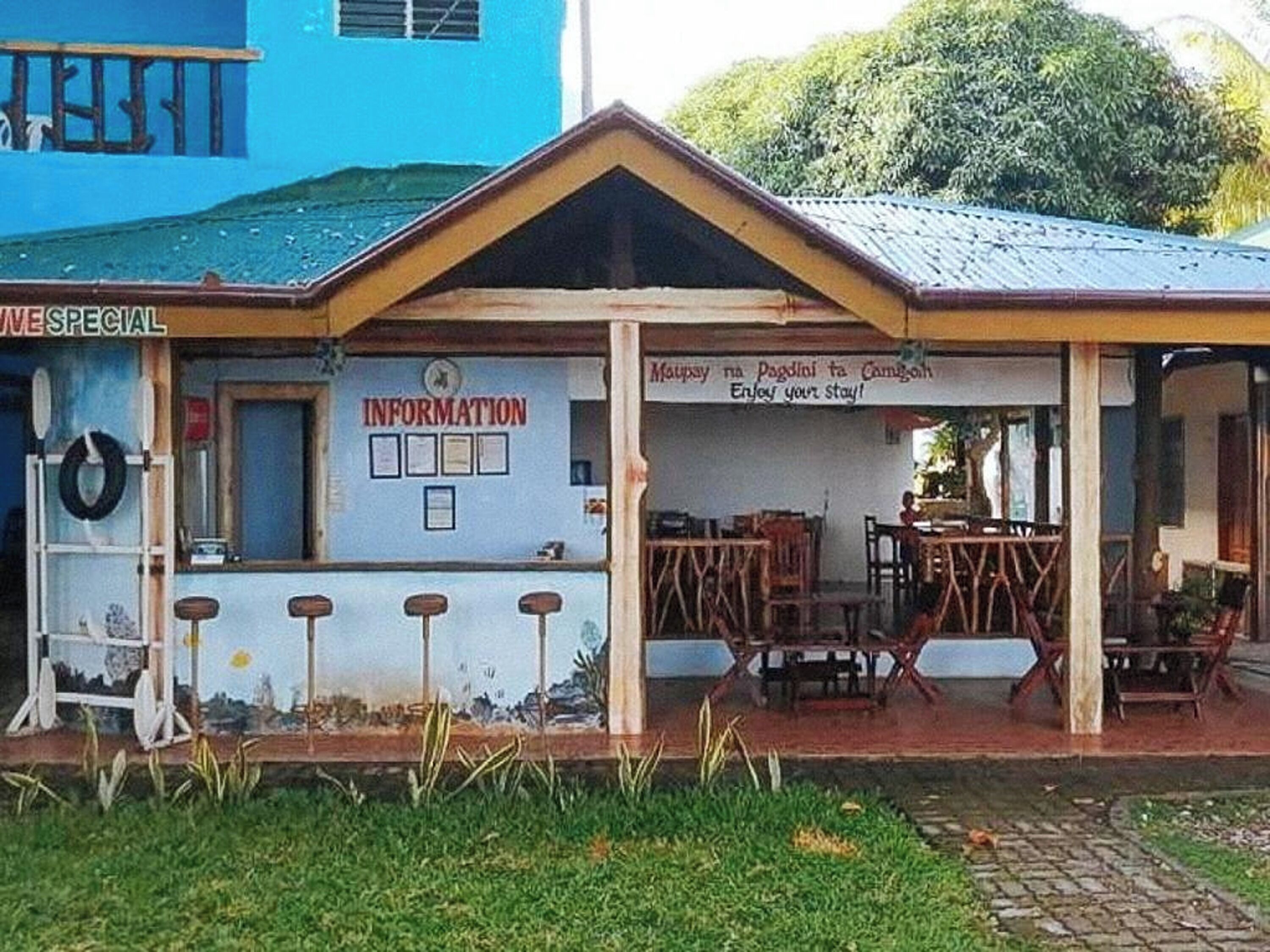 Un edificio con fachada azul, un cartel que dice “INFORMATION” y una zona de bar con taburetes y mesas.