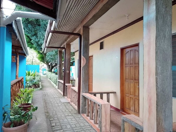 A covered corridor with potted plants, wooden benches, and a tiled floor. - July'S Haven Seaside Pension Camiguin (Mambajao)