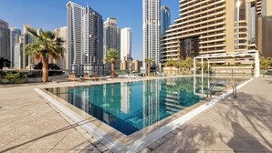 Une piscine entourée de bâtiments de grande hauteur, avec des chaises longues et des palmiers.