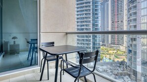 Un balcon avec une table et des chaises, une paroi en verre et une vue sur des immeubles de grande hauteur et des chantiers de construction.