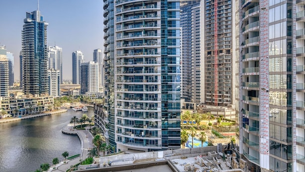 Un immeuble de grande hauteur doté de nombreux balcons, une rivière au premier plan et d’autres immeubles de grande hauteur en arrière-plan.
