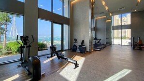 Een moderne fitnessruimte met cardioapparatuur, een roeimachine en een loopband. Grote ramen bieden uitzicht op een stadslandschap en een brug.