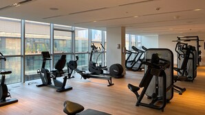 Ett modernt gym med olika typer av träningsutrustning, stora fönster och utsikt över staden.