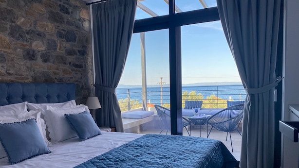 A bedroom with a large bed, a stone wall, and a balcony with a view of the sea. - Aélia Stone Houses in Nies (Almyros)