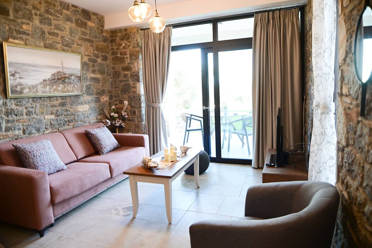 A cozy living room with a stone wall, a sofa, a coffee table with candles, and a view through a glass door.