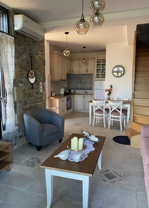 A cozy living room with a grey armchair, a wooden coffee table with candles, and a dining area with white chairs and a vase of flowers.