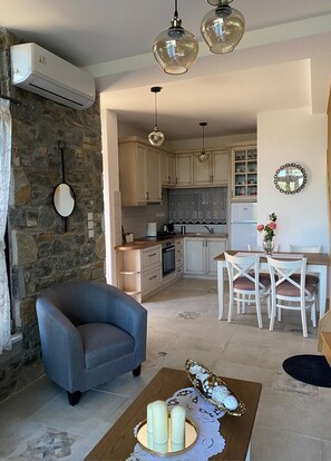 A modern kitchen with stone walls, a dining area with white chairs, and a blue armchair.