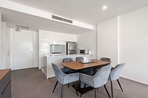 A modern kitchen with white cabinets, a central island, and a dining area with a wooden table and grey upholstered chairs. - Spacious Lakefront Apartment with Pool Access (Kingston)
