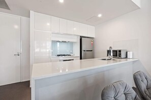 A modern kitchen with white cabinetry, a stainless steel refrigerator, a gas stove, and a microwave.