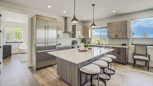 A modern kitchen with a large island, stainless steel appliances, pendant lighting, and a view of the outdoors.