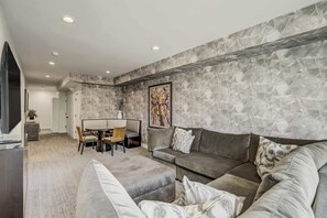 Una sala moderna con un sofá gris, una zona de comedor con mesa y sillas, y una pared con diseño de piedra.