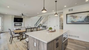 A modern kitchen with a central island, pendant lighting, and a dining area with a staircase leading to an upper level.