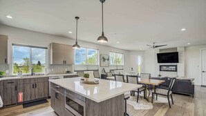 A modern kitchen with a large island, pendant lighting, and a dining area with a TV and seating.