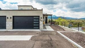 A modern two-story building with a garage, a covered patio, and a view of mountains.